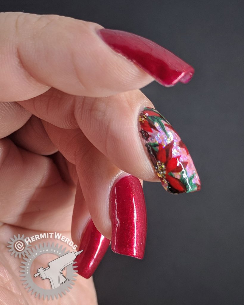 Glittery Poinsettia - Hermit Werds - red manicure with a pink accent nail covered with iridescent glitter and freehand painted holly leaves and poinsettia flowers (Robin Moses)