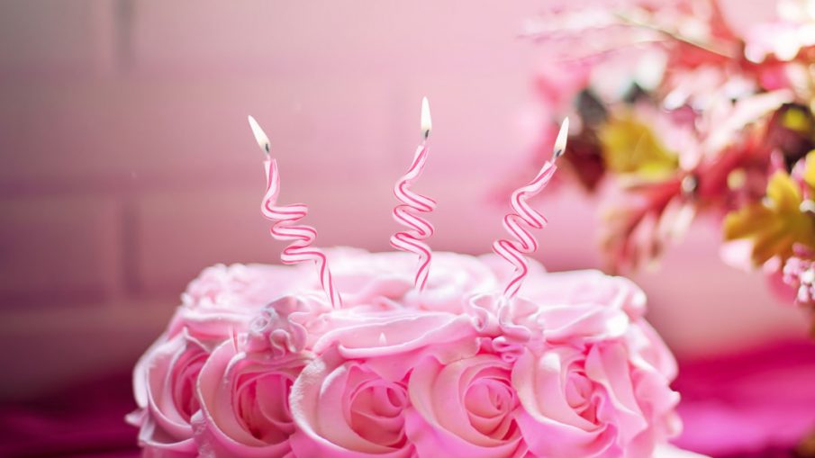 Pink cake with three fancy candles sticking out of it.