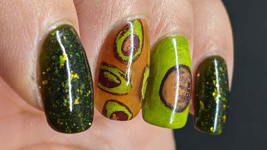 A rich green mani with two accent nails. The first has a brown jelly base and many small avocado decals and the second is a closeup of an avocado with the pit showing.