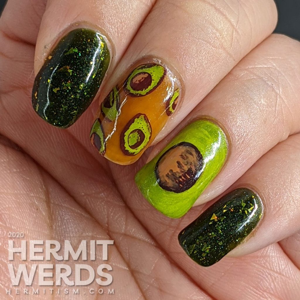 A rich green mani with two accent nails. The first has a brown jelly base and many small avocado decals and the second is a closeup of an avocado with the pit showing.