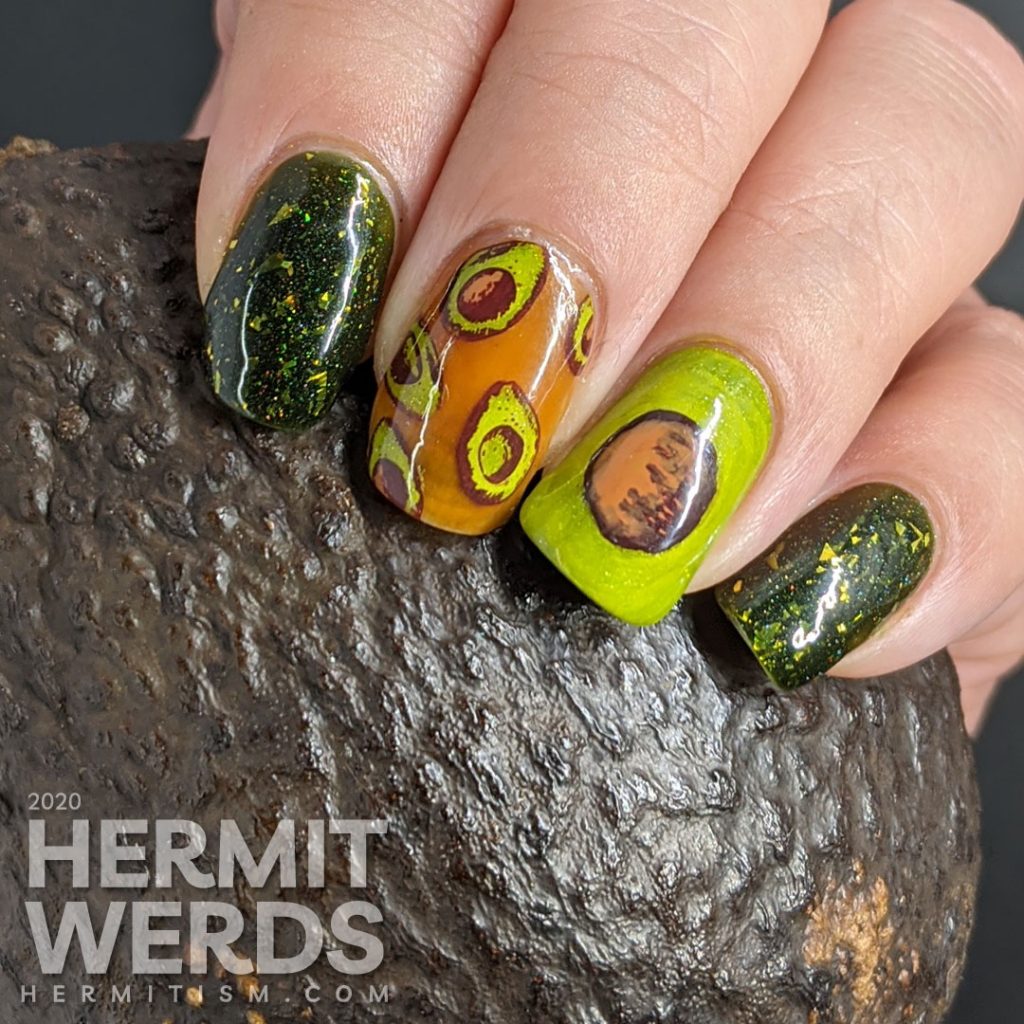 A rich green mani with two accent nails. The first has a brown jelly base and many small avocado decals and the second is a closeup of an avocado with the pit showing.