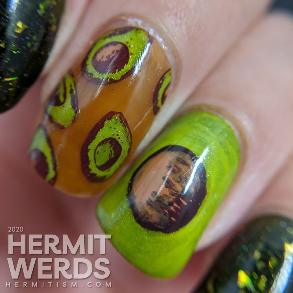 A rich green mani with two accent nails. The first has a brown jelly base and many small avocado decals and the second is a closeup of an avocado with the pit showing.