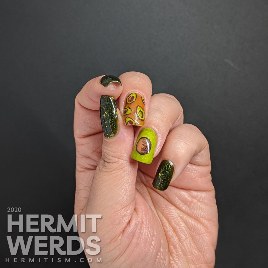 A rich green mani with two accent nails. The first has a brown jelly base and many small avocado decals and the second is a closeup of an avocado with the pit showing.