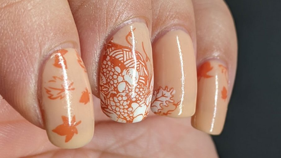 A simple fall nail art with stampings of leaves, pumpkins, and other harvest-related items on an apricot jelly polish background.