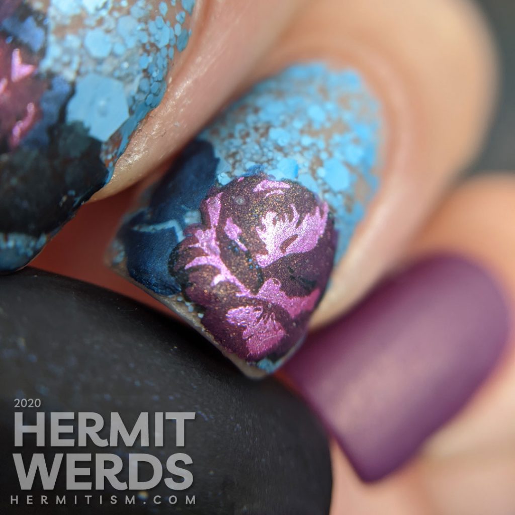 Purple and blue rose-themed nail art with layered stamping roses on a matte blue glitter background.