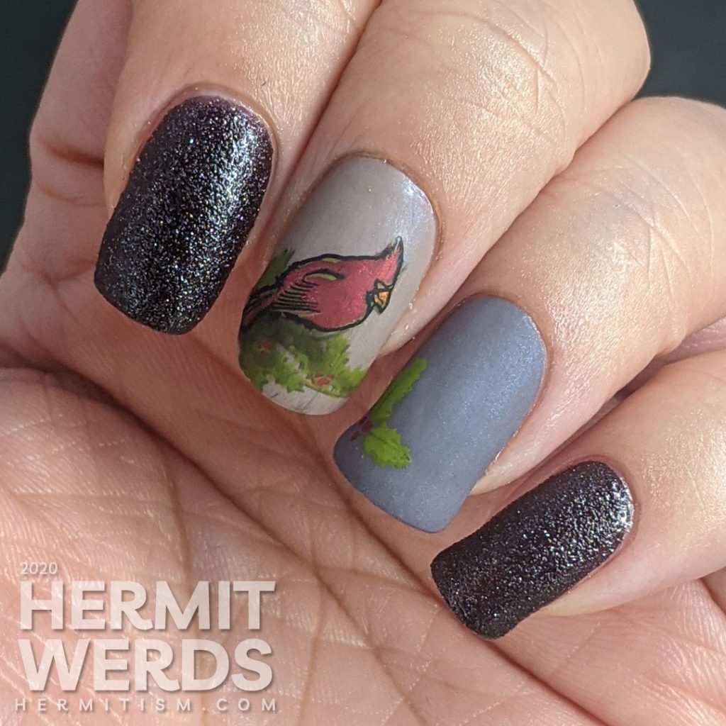 A winter nail art with dusty purple polish and bright red cardinal and holly stamping decals on top.