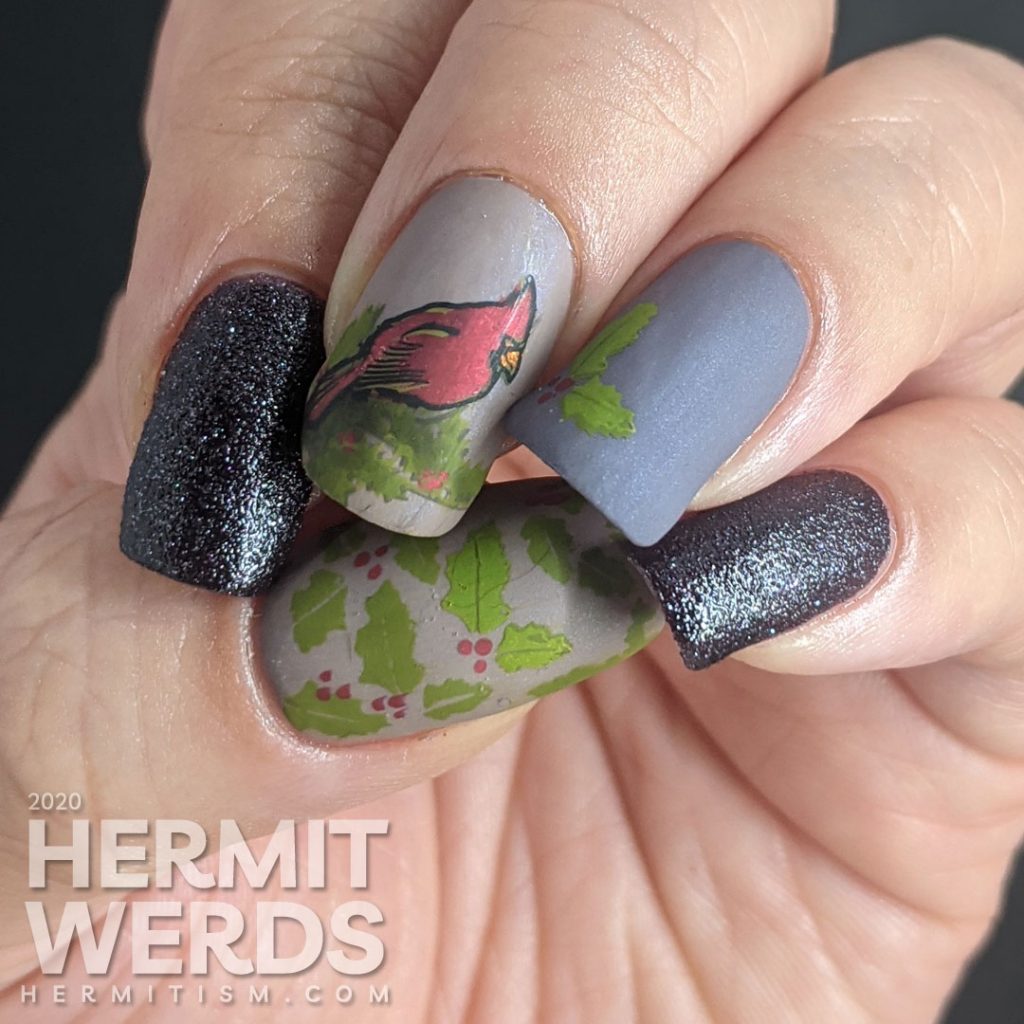 A winter nail art with dusty purple polish and bright red cardinal and holly stamping decals on top.