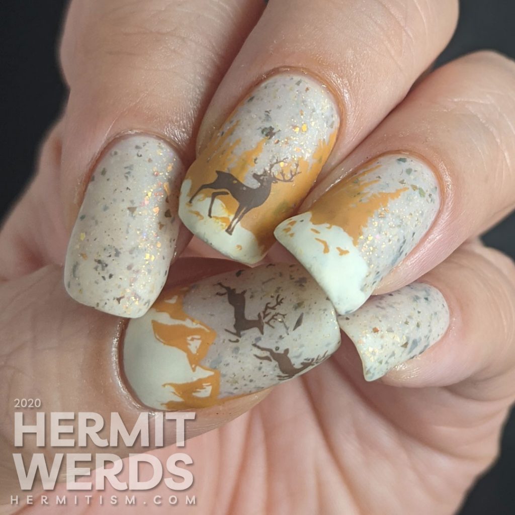 Nail art of a wintery scene with pine trees, mountains, and magical deer on a light tan flakie-filled polish base.