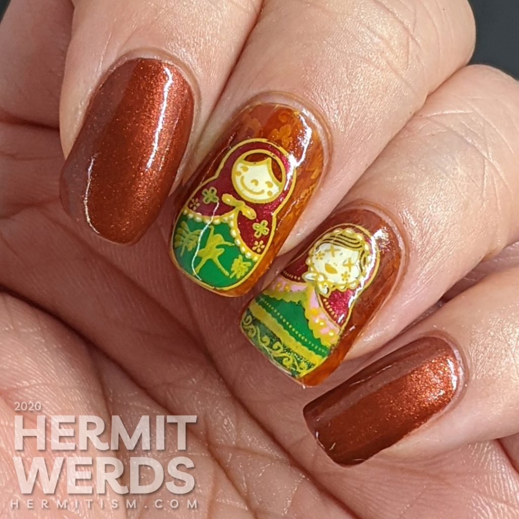 Nail art with stamping decals of beautiful Russian nesting dolls or matryoshka dolls in pinks, reds, and greens on a rusty red background with subtle jelly sandwich.