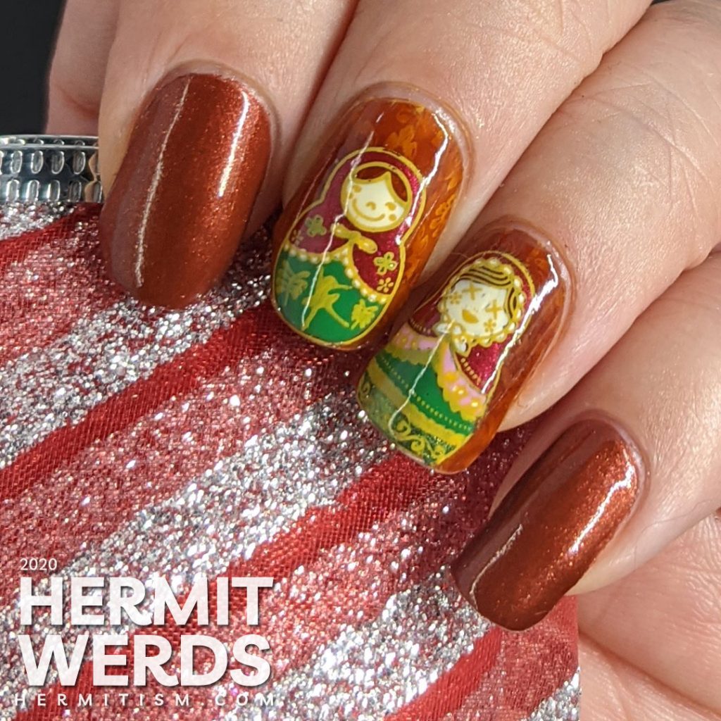 Nail art with stamping decals of beautiful Russian nesting dolls or matryoshka dolls in pinks, reds, and greens on a rusty red background with subtle jelly sandwich.