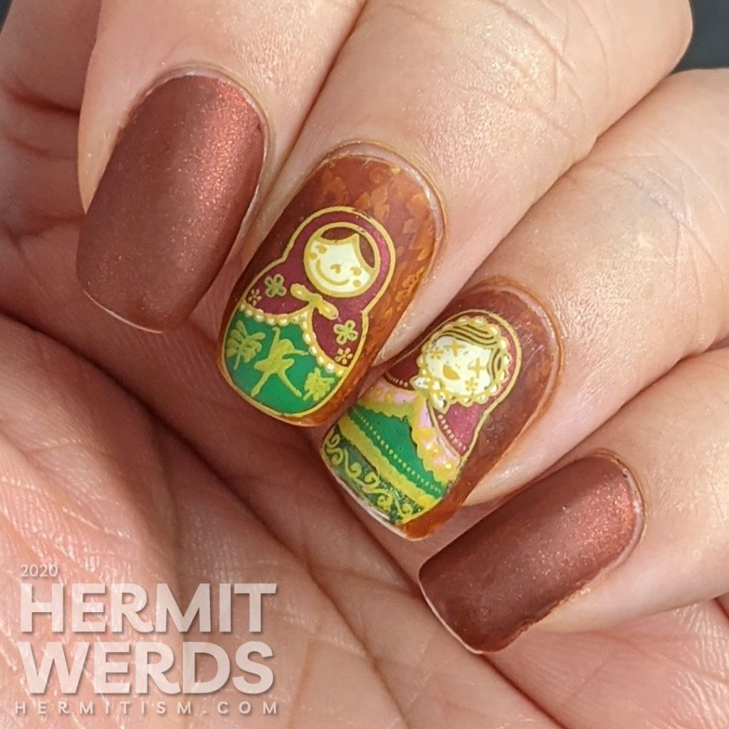 Nail art with stamping decals of beautiful Russian nesting dolls or matryoshka dolls in pinks, reds, and greens on a rusty red background with subtle jelly sandwich.