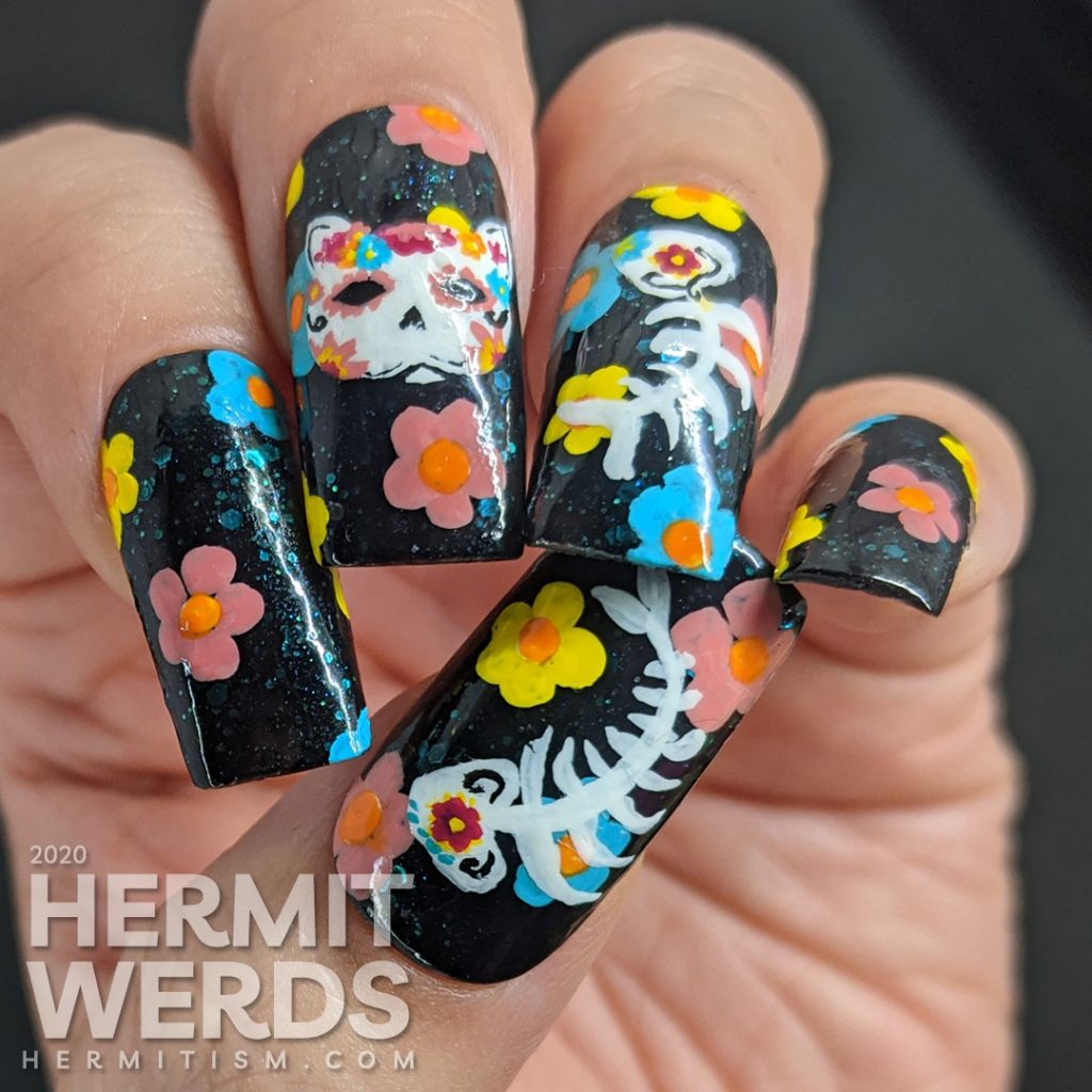 Sugar skull nail art for the Day of the Dead on black jelly teal glitter fake nails with freehand painted cat and fish sugar skulls and flowers.