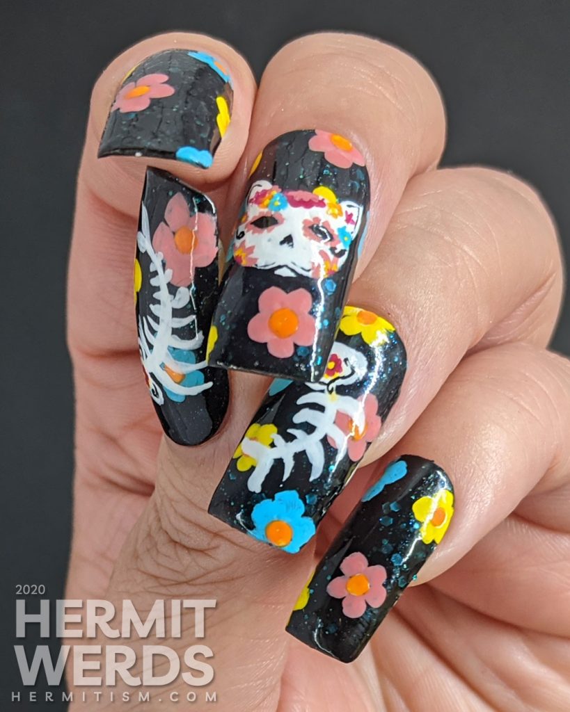 Sugar skull nail art for the Day of the Dead on black jelly teal glitter fake nails with freehand painted cat and fish sugar skulls and flowers.