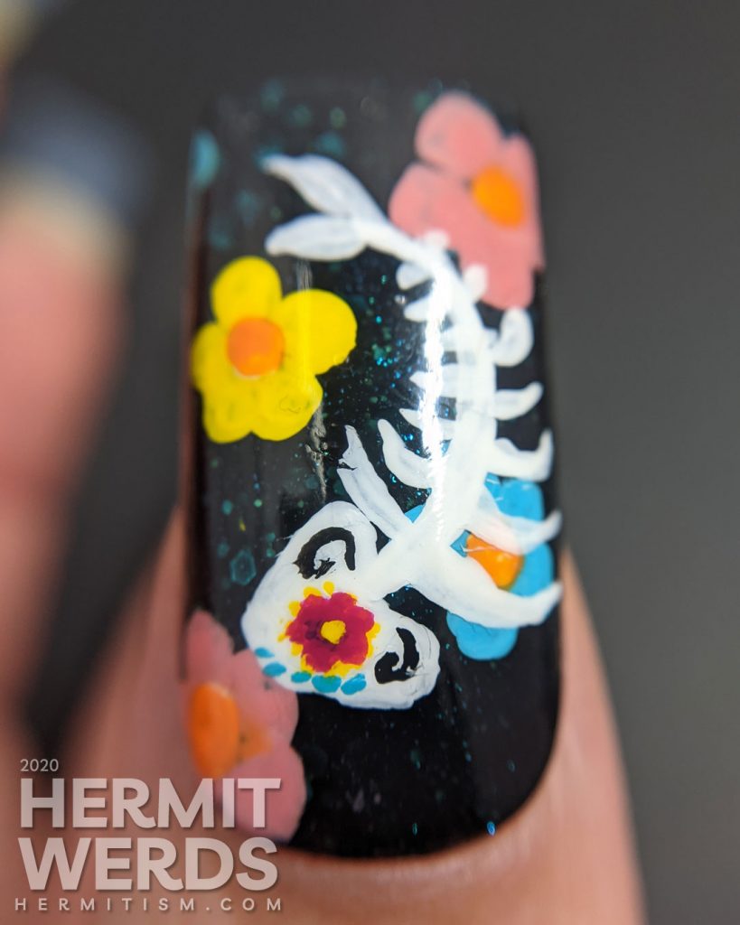 Sugar skull nail art for the Day of the Dead on black jelly teal glitter fake nails with freehand painted cat and fish sugar skulls and flowers.