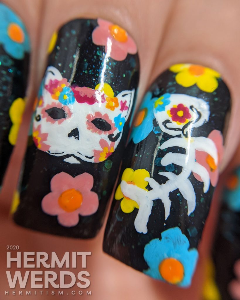 Sugar skull nail art for the Day of the Dead on black jelly teal glitter fake nails with freehand painted cat and fish sugar skulls and flowers.