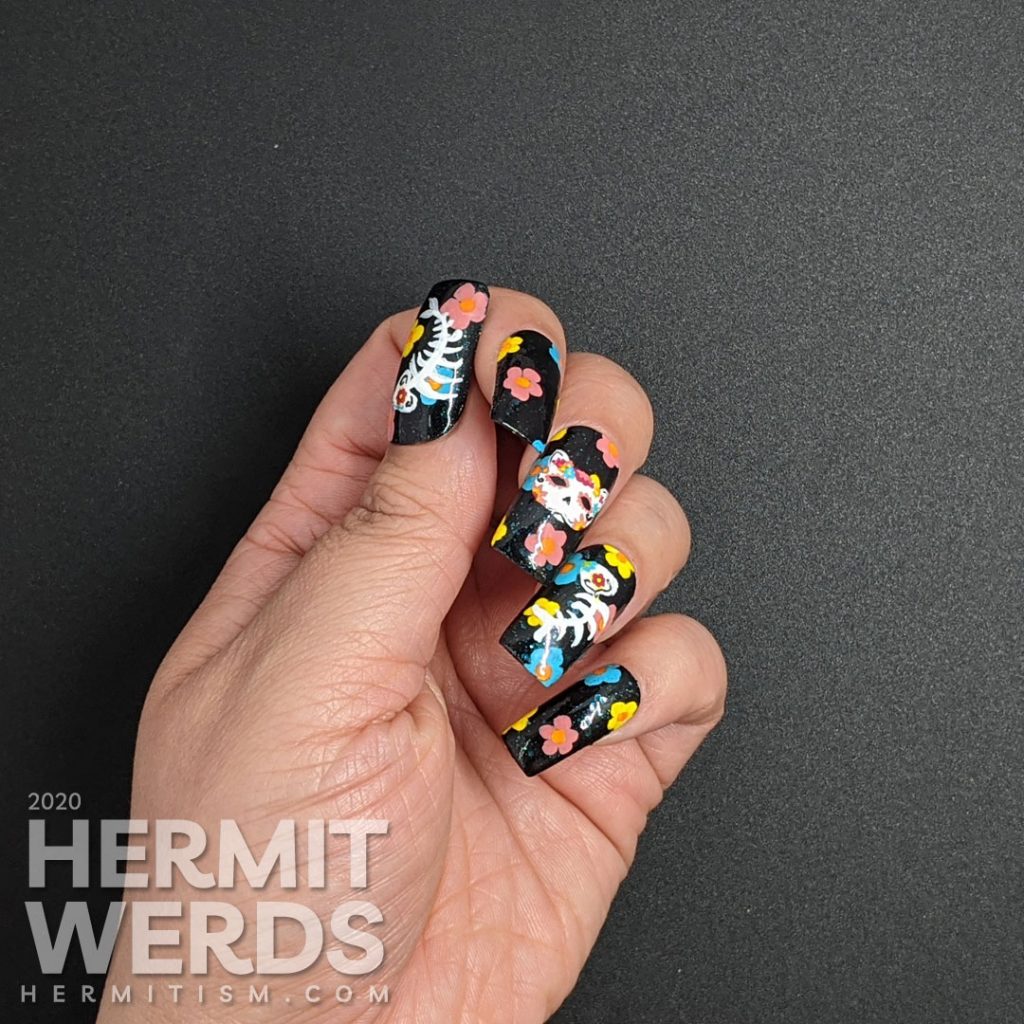 Sugar skull nail art for the Day of the Dead on black jelly teal glitter fake nails with freehand painted cat and fish sugar skulls and flowers.