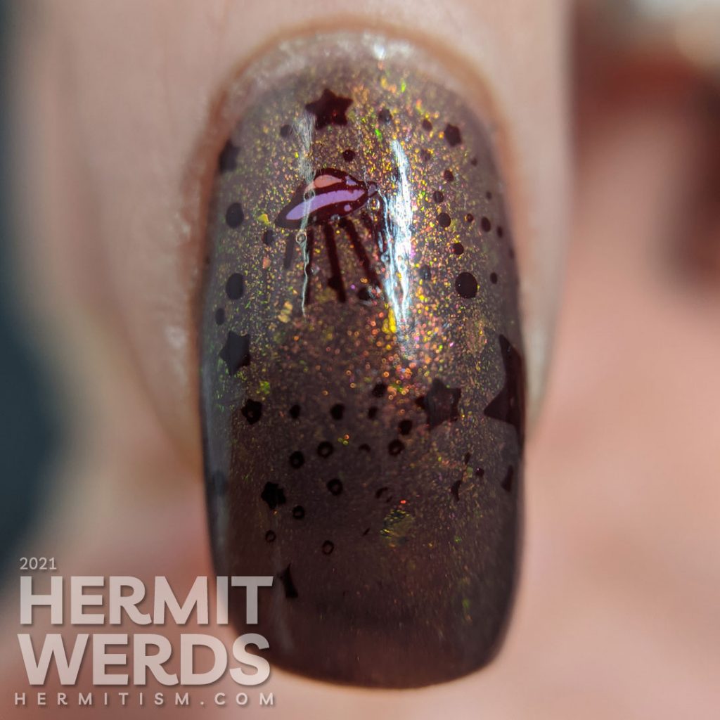 A muted red nail art with a science fiction theme. Cute aliens stamping decals scream at each other while an astronaut says "hi".
