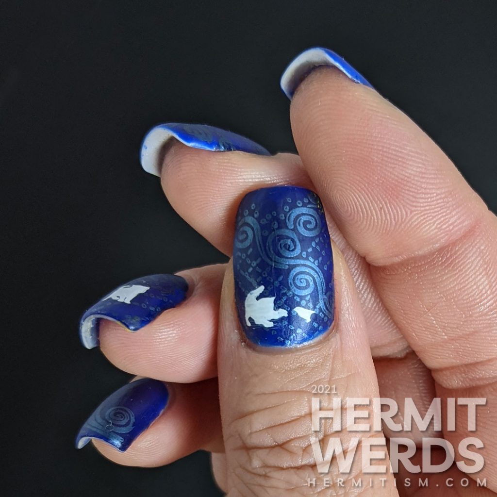 A dark blue nail art with metallic blue decorative swirls stamped in the background and little white cat silhouette stamping decals.