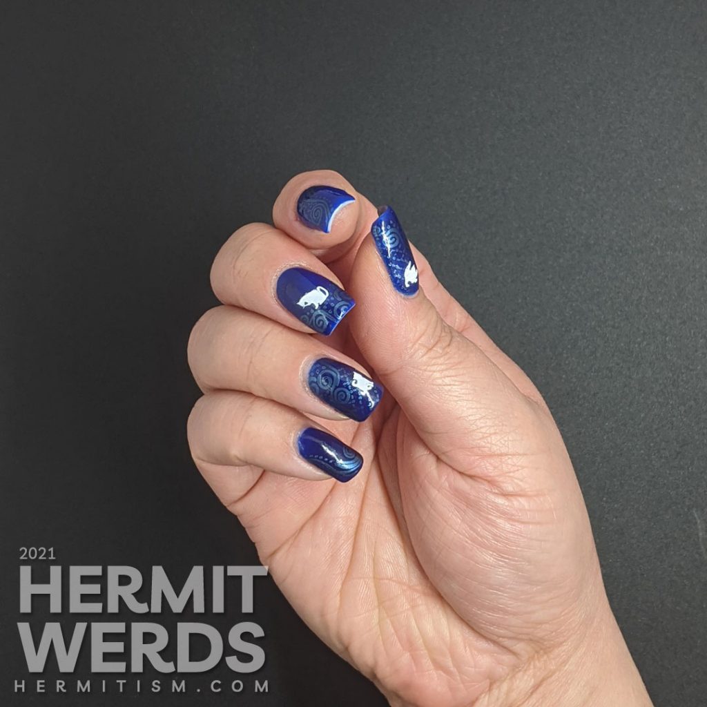 A dark blue nail art with metallic blue decorative swirls stamped in the background and little white cat silhouette stamping decals.