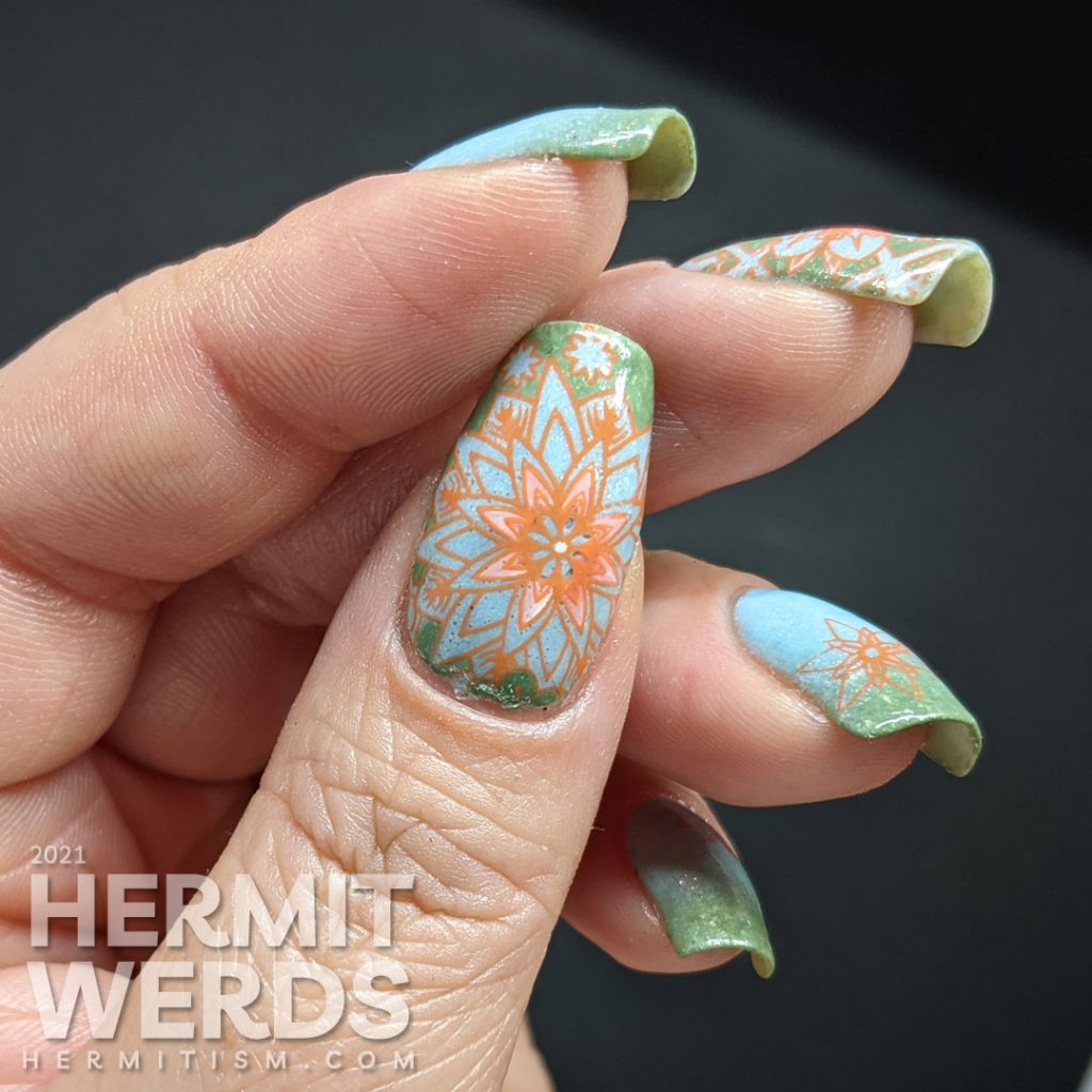 A pastel wintery nail art with snowflake-like flower stamping decals in green, aqua, and orange.