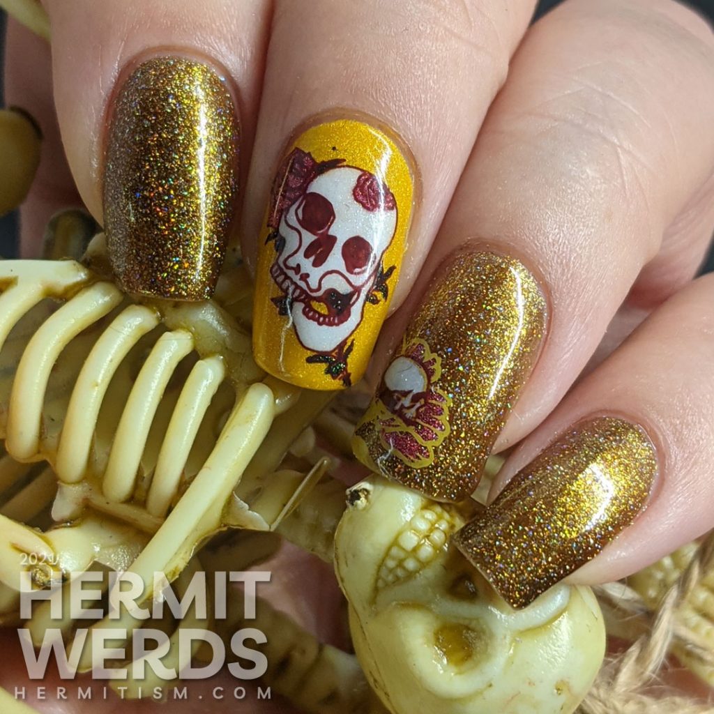 A scattered holographic mustard nail art design with tattoo-like skulls, florals, and rib cage stamping decals.
