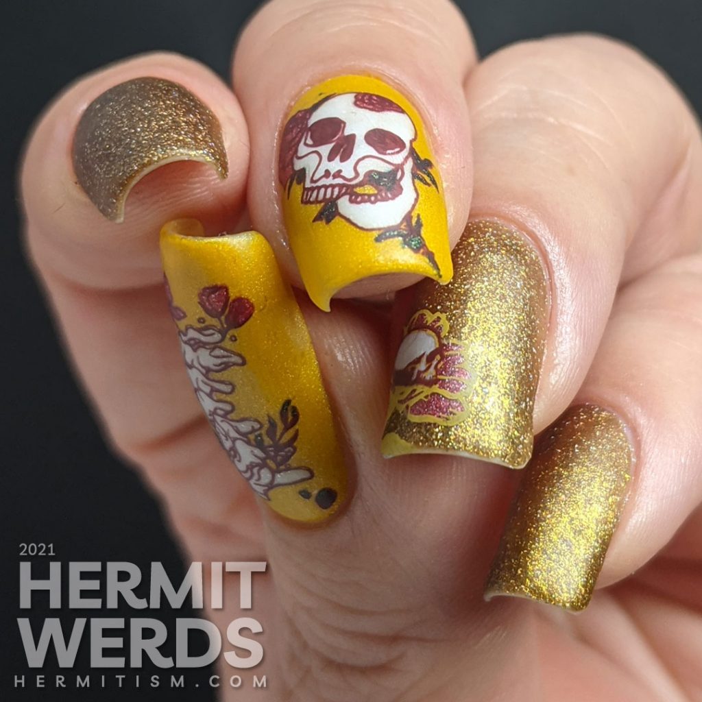 A scattered holographic mustard nail art design with tattoo-like skulls, florals, and rib cage stamping decals.