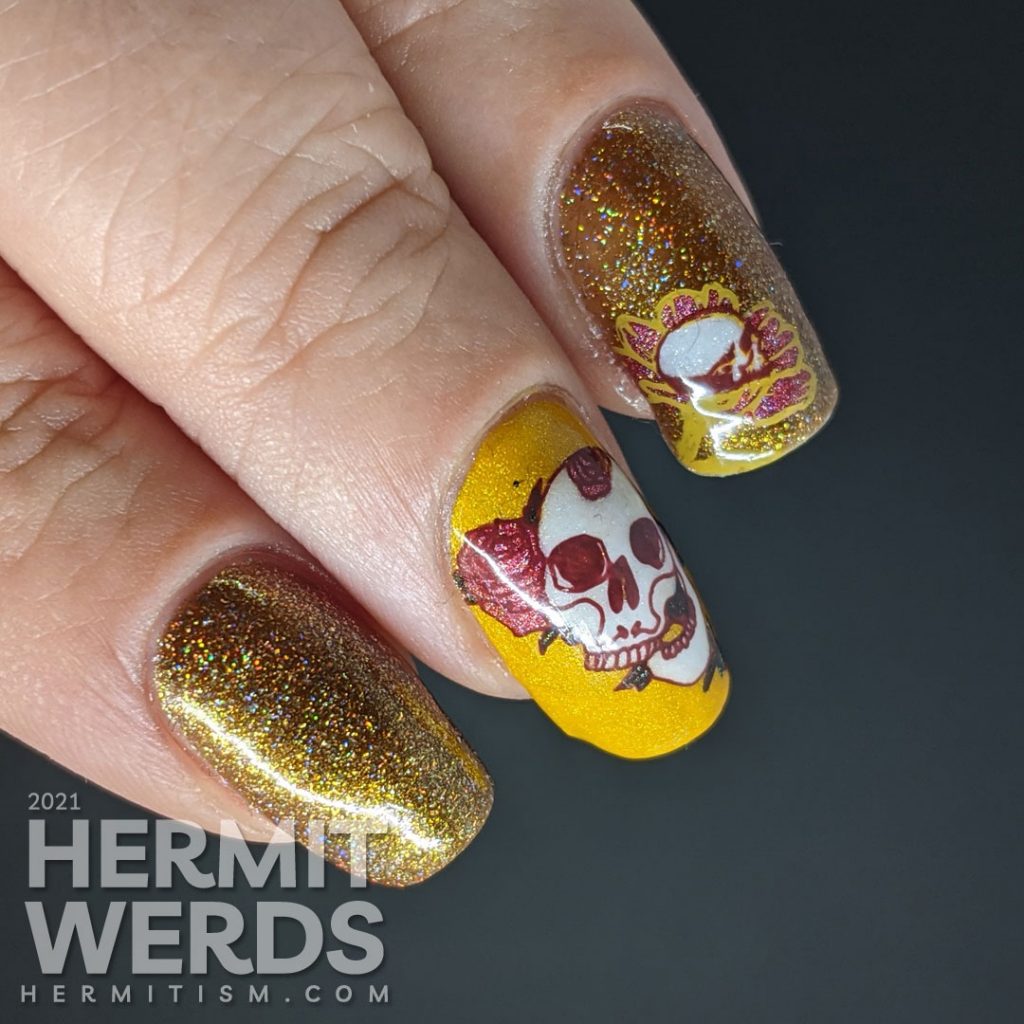 A scattered holographic mustard nail art design with tattoo-like skulls, florals, and rib cage stamping decals.