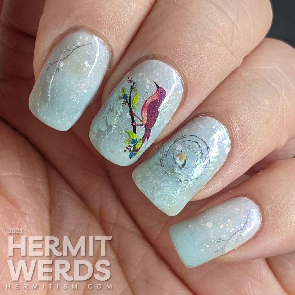 Bird nail art with red bird, robin, and bluebird water decals placed on a white and blue thermal polish with shimmering ferns stamped on top.