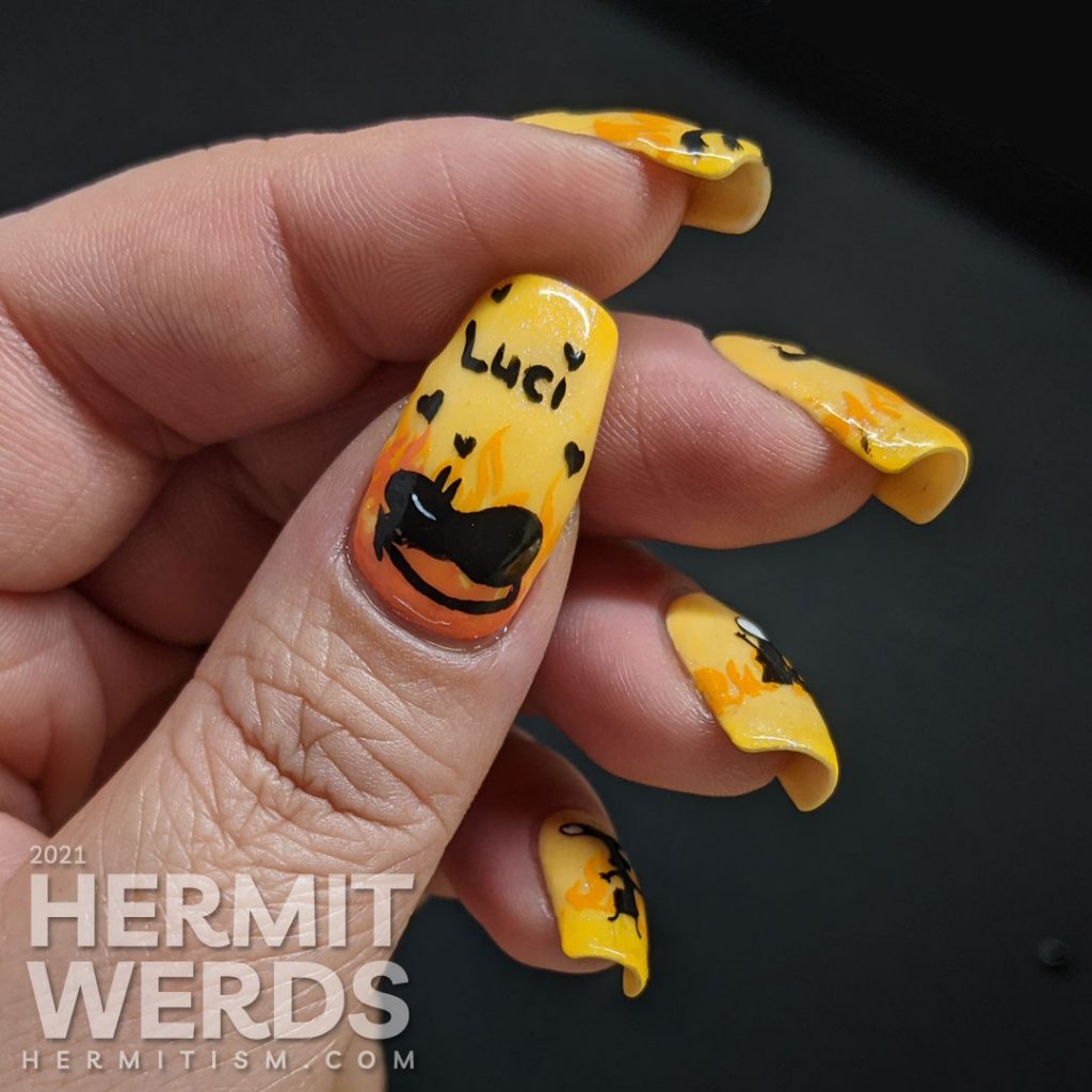 Yellow and orange nail art with the demon Luci (cat) from Netflix's Disenchanted freehand painted on top of flames.