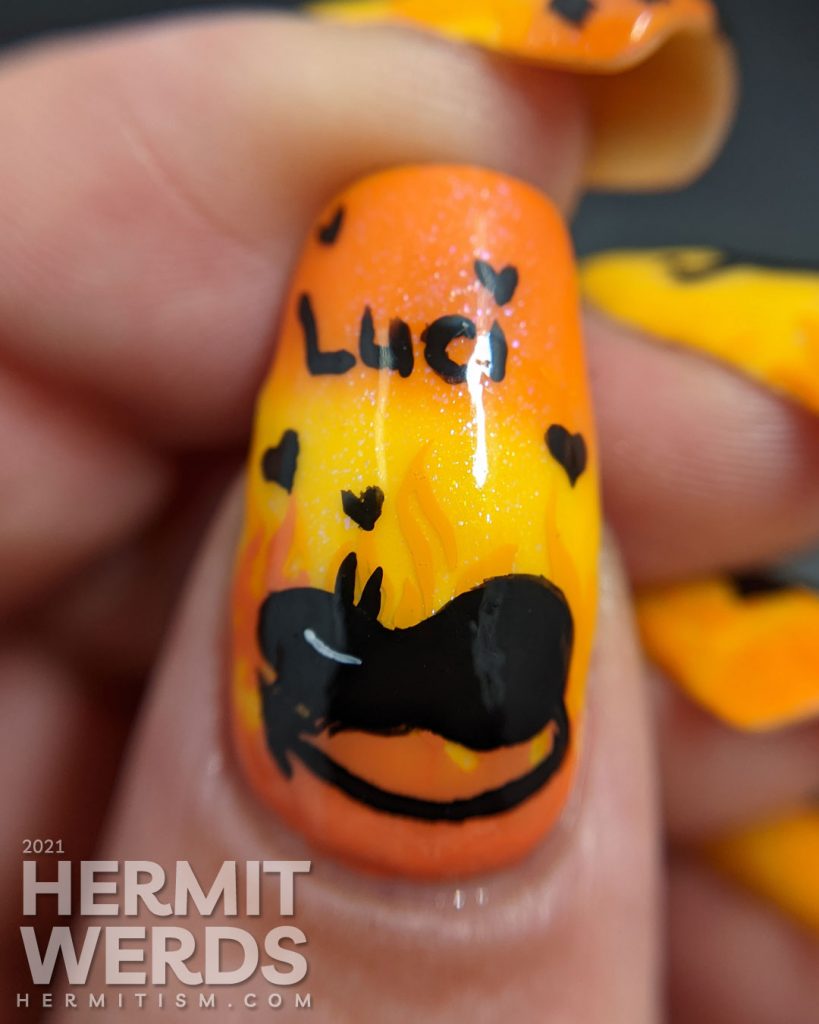 Yellow and orange nail art with the demon Luci (cat) from Netflix's Disenchanted freehand painted on top of flames.