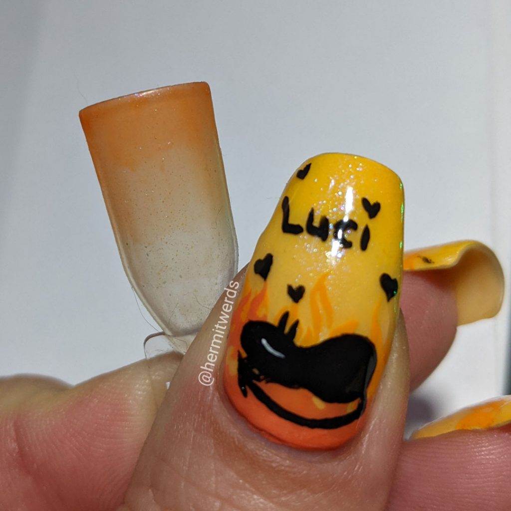 Yellow and orange nail art with the demon Luci (cat) from Netflix's Disenchanted freehand painted on top of flames.