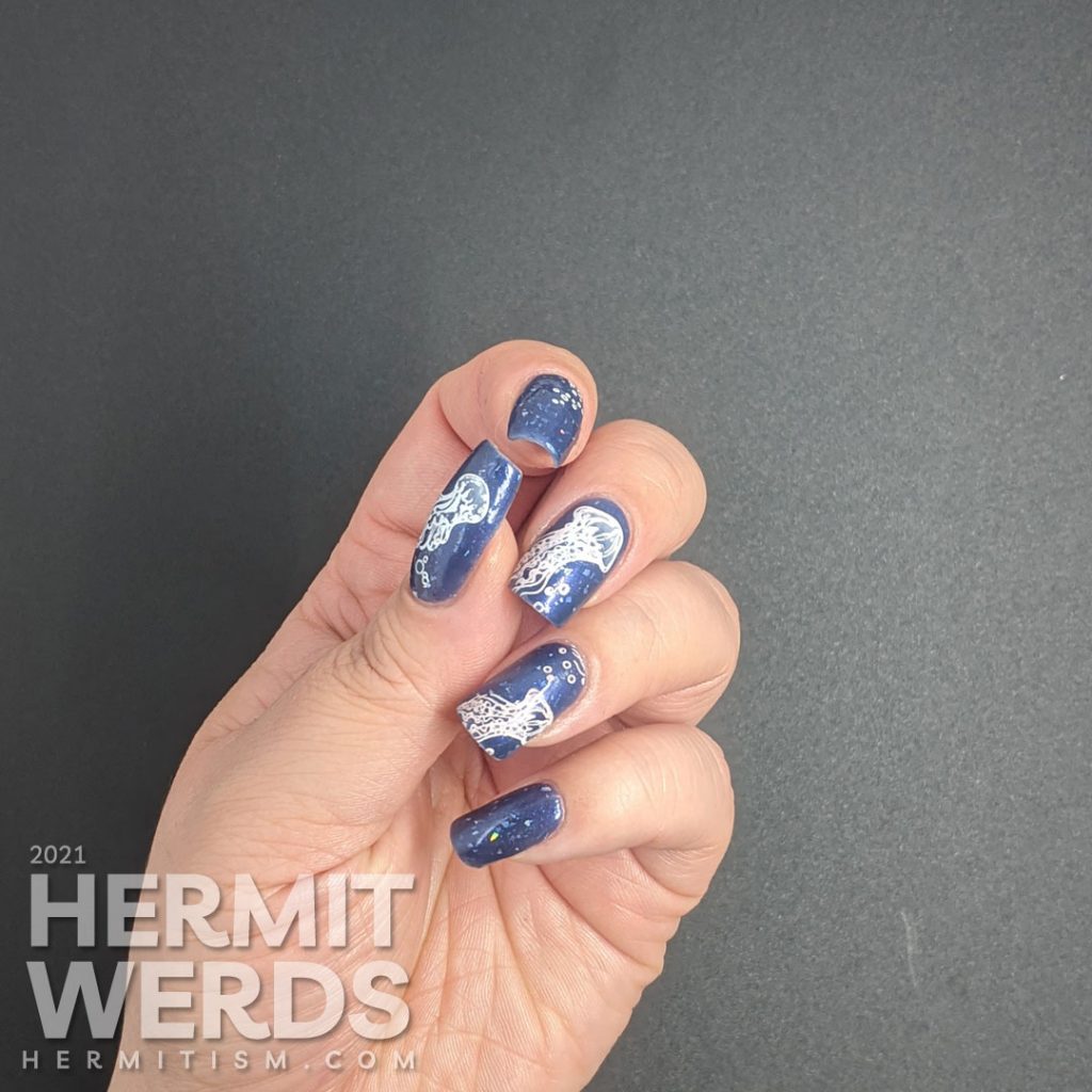 A dusty dark blue mani with transparent jellyfish stamping decals swimming in the sea with little bubbles and flashes of holo.