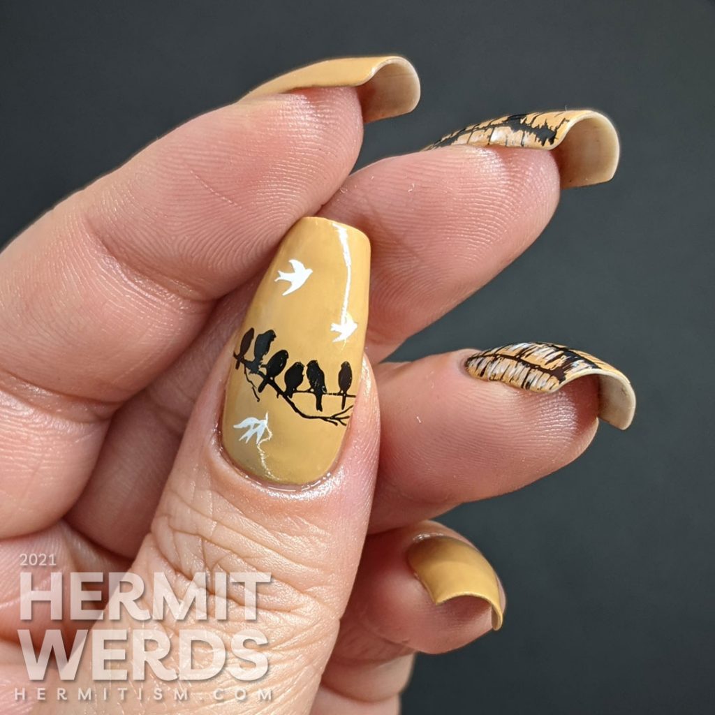 A tan nail art with birch tree trunk stamping images highlighted with white nail polish and frolicking birds.