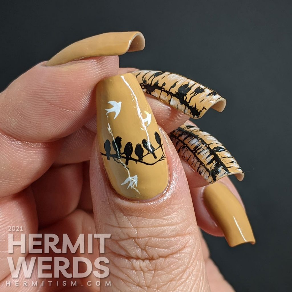 A tan nail art with birch tree trunk stamping images highlighted with white nail polish and frolicking birds.