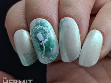 A pearly grey nail art with a soft swirl of green and stamping image of a dandelion puff on top. Done on false nails.