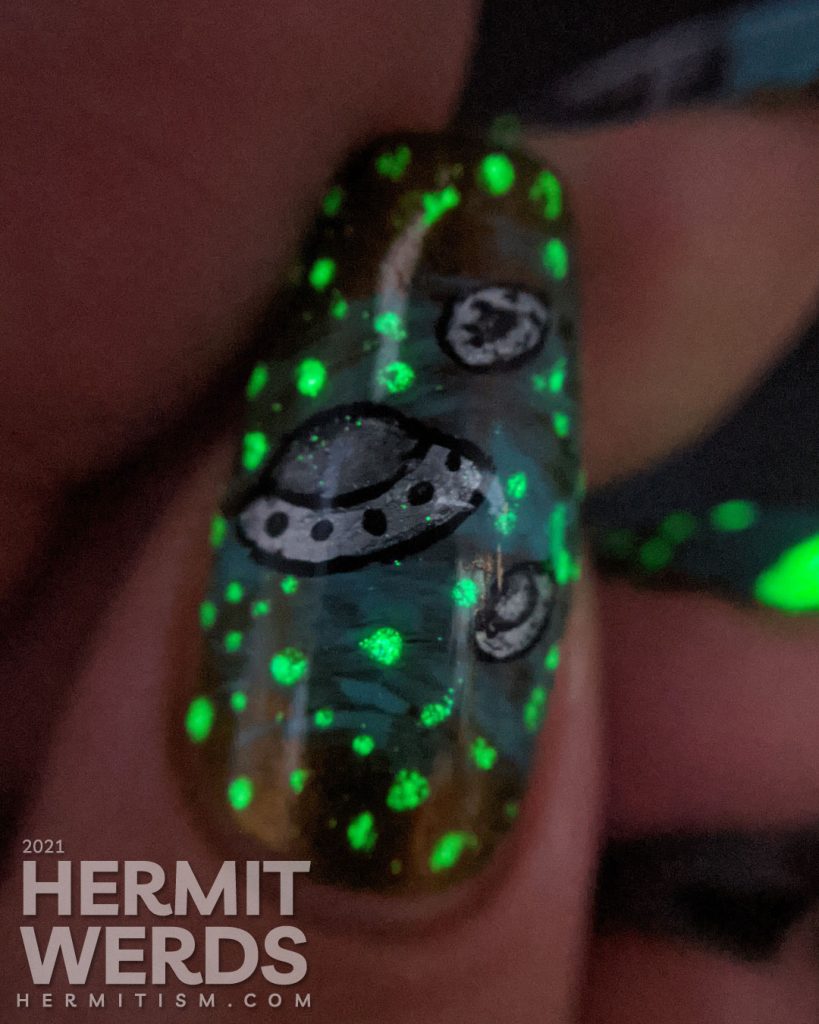 A freehand UFO nail art design with an multichrome olive/red and blue sky, silver UFO with glow in the dark tractor beam and stars.