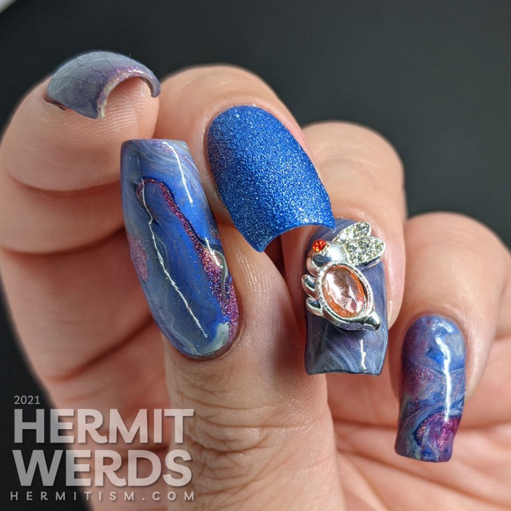 A blurple, blue, and grey with pink highlights fluid art nail design with a pink and silver bunny nail charm as accent.