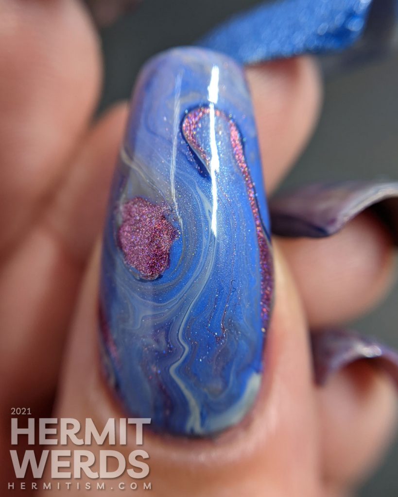 A blurple, blue, and grey with pink highlights fluid art nail design with a pink and silver bunny nail charm as accent.