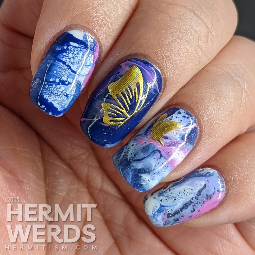 A fluid art nail art decorated with holographic gold butterfly stickers in blue, blurple, lavender, and white.