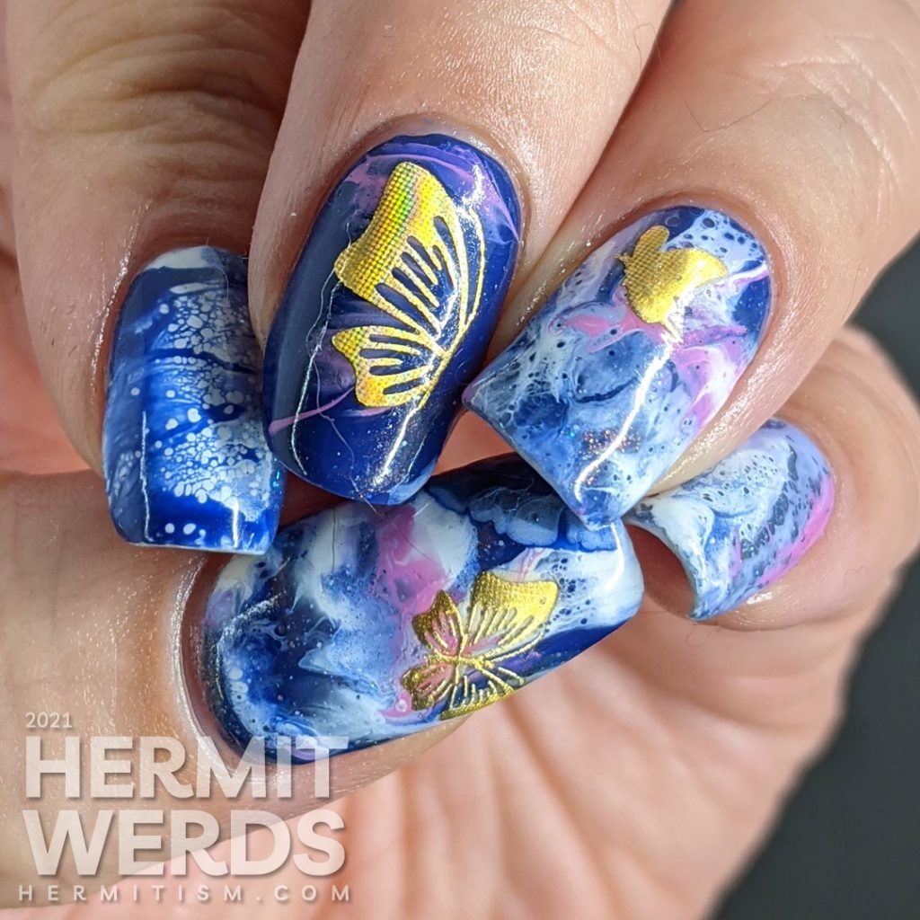 A fluid art nail art decorated with holographic gold butterfly stickers in blue, blurple, lavender, and white.