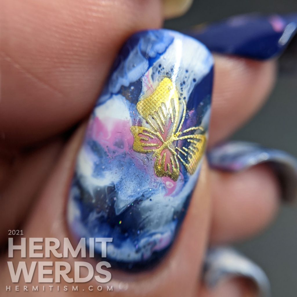 A fluid art nail art decorated with holographic gold butterfly stickers in blue, blurple, lavender, and white.