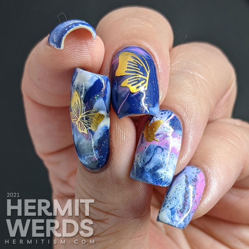 A fluid art nail art decorated with holographic gold butterfly stickers in blue, blurple, lavender, and white.