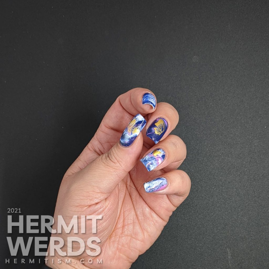 A fluid art nail art decorated with holographic gold butterfly stickers in blue, blurple, lavender, and white.