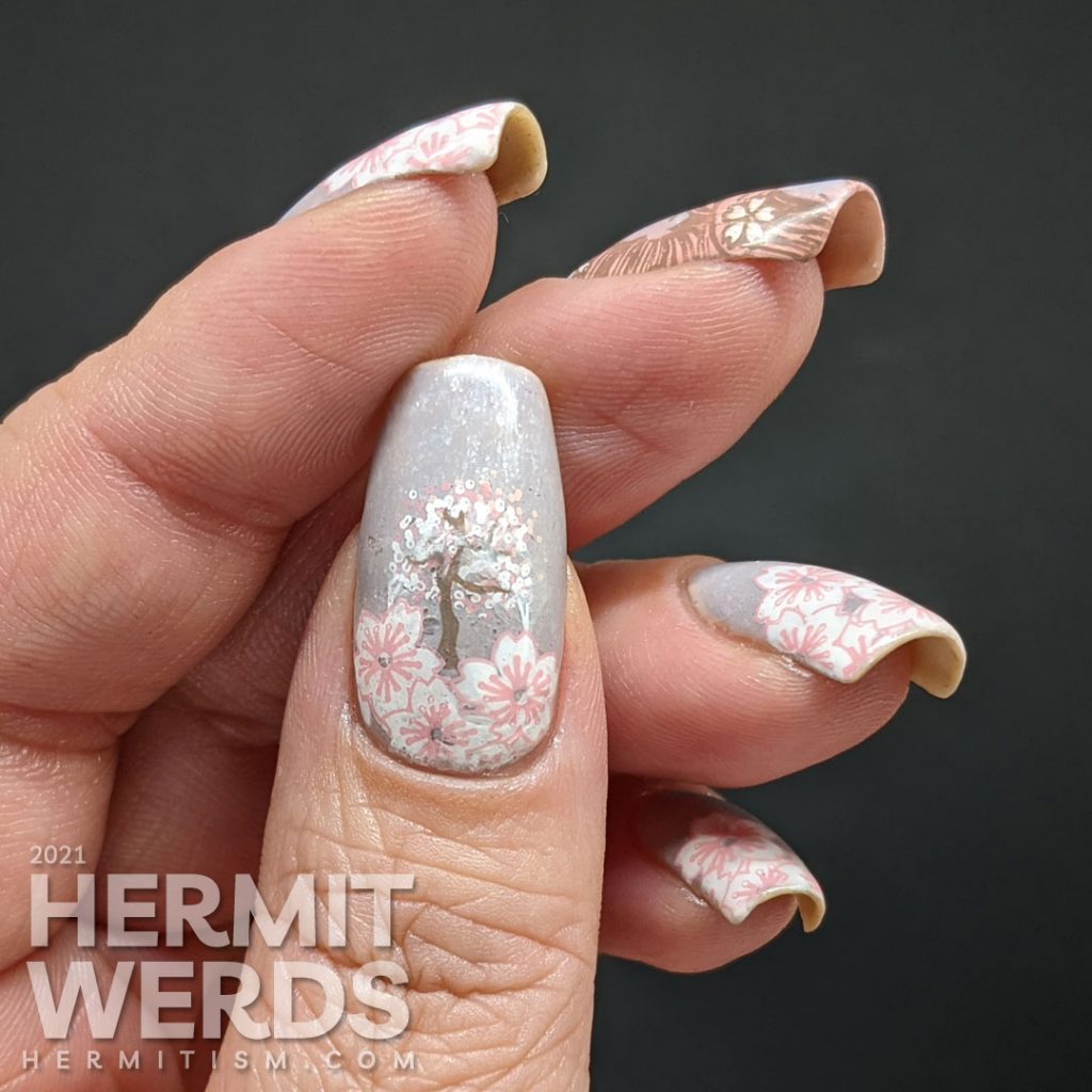 A soft grey nail art with stamping decals of sakura blossom French tips a pink-haired woman with more flowers and a blooming cherry tree.