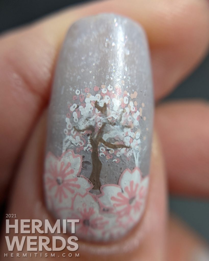 A soft grey nail art with stamping decals of sakura blossom French tips a pink-haired woman with more flowers and a blooming cherry tree.