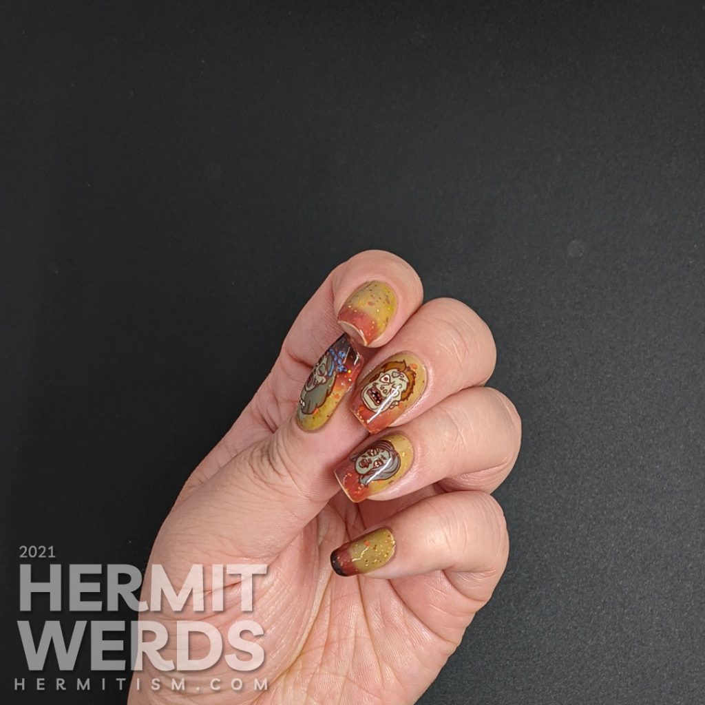 Zombie nail art with cartoon zombie head stamping decals and on a mustard/orange/brown tri-thermal base with orange and gold glitters.