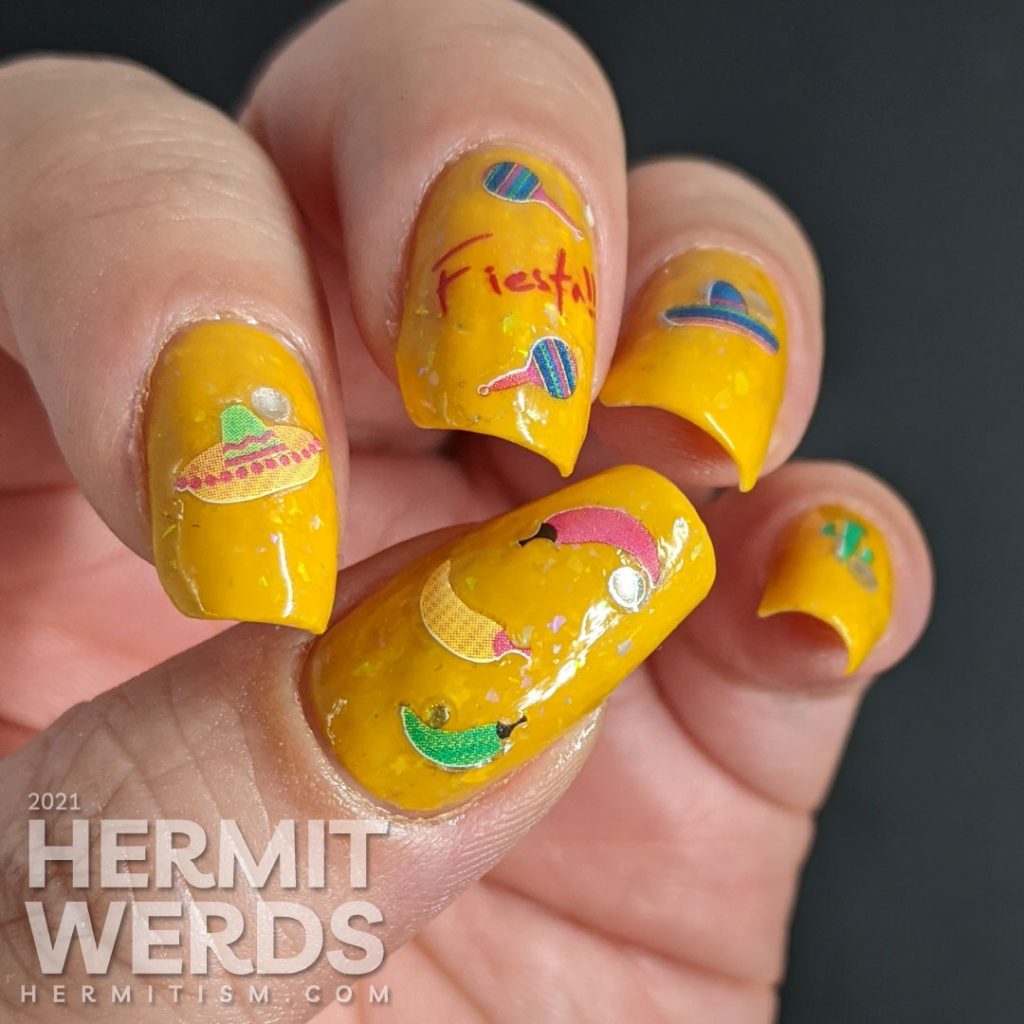 Mexico-related nail stickers (hot peppers, sombreros, maracas, and a cactus) with the word "fiesta" decorating a bright mustard crelly with iridescent flakes to celebrate Cinco de Mayo.