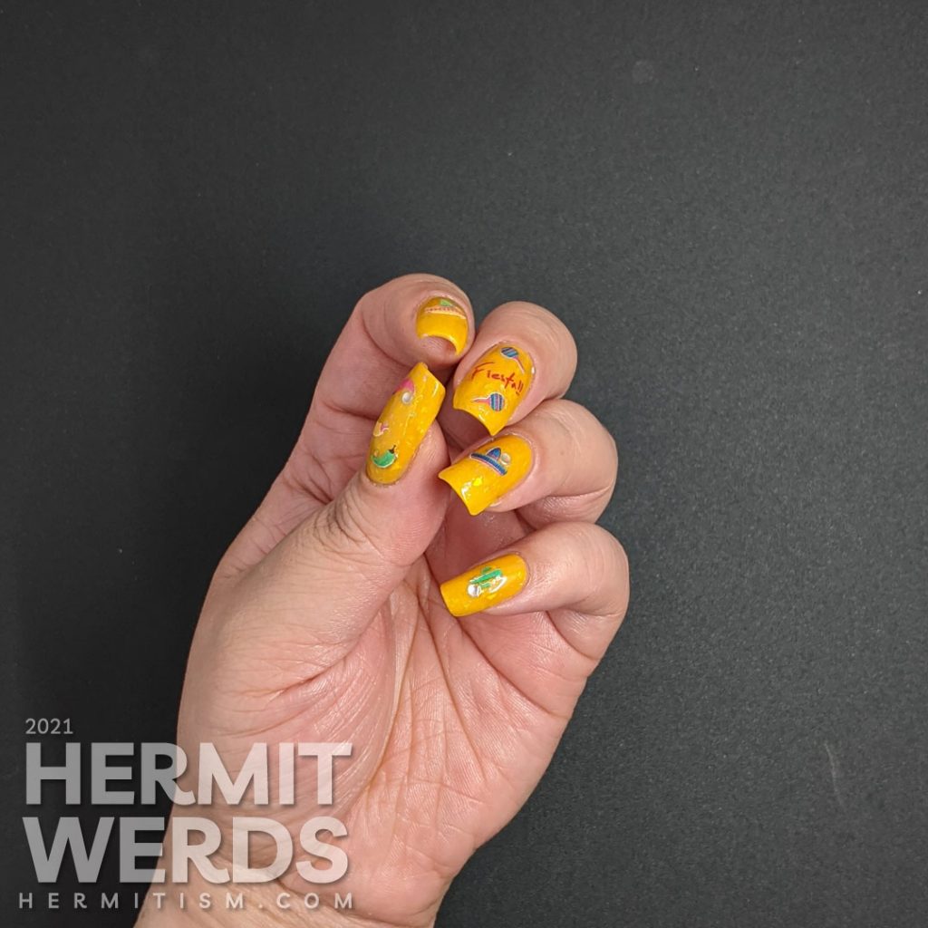 Mexico-related nail stickers (hot peppers, sombreros, maracas, and a cactus) with the word "fiesta" decorating a bright mustard crelly with iridescent flakes to celebrate Cinco de Mayo.