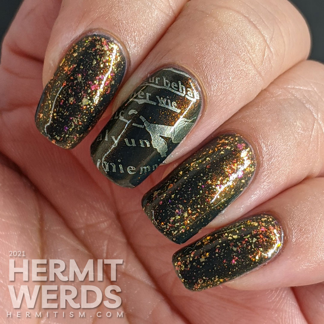 A smoky navy blue multichrome nail art with fake writing being highlighted (alphabet) stamping decals topped with a gold/iridescent topper.