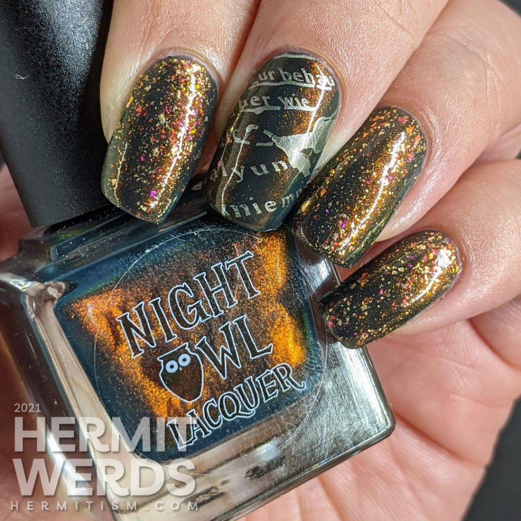 A smoky navy blue multichrome nail art with fake writing being highlighted (alphabet) stamping decals topped with a gold/iridescent topper.